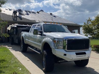 White pickup truck parked by a house while workers repair the roof
