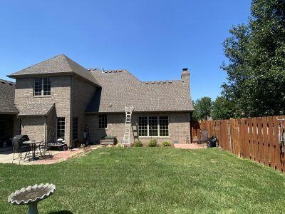 Backyard with green lawn, brick two-story house, patio furniture, and wooden fence under a blue sky