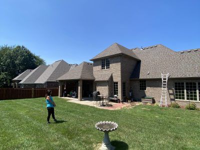 Backyard with a brick house, green lawn, and a child standing near a birdbath under a clear blue sky