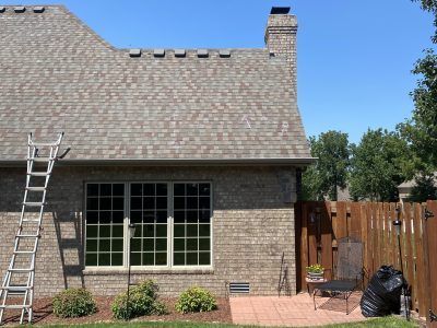 Backyard patio beside a brick house, with a ladder, large window, and wooden fence under a blue sky