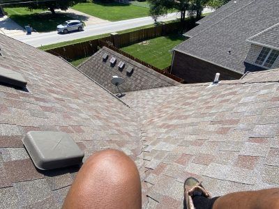 Looking down a shingled roof from a rooftop, with a shoe and knee visible in the foreground.