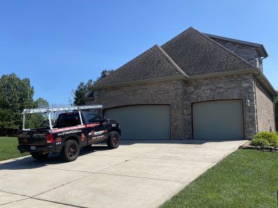 Black pickup truck parked in a driveway in front of a two-car brick garage under a clear blue sky