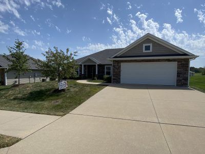 Suburban single-story house with two-car garage, driveway, and small front yard under a blue sky