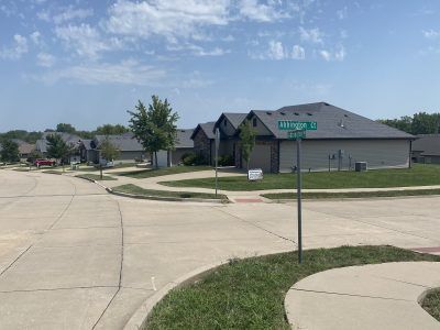 Suburban street corner with houses, sidewalk, and a gray building under a blue sky.