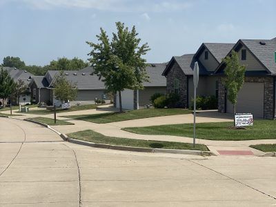 Quiet suburban street with row houses, lawns, trees, and a curved sidewalk under clear sky