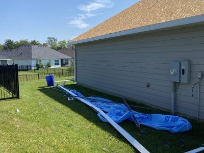 Blue tarp and white PVC pipe lying on a grassy yard beside a house with a gray utility box.