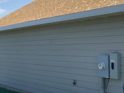 Gray-sided building exterior with electrical meter boxes mounted near the roofline