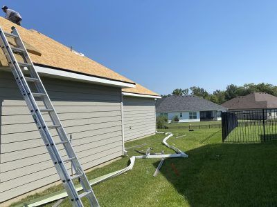 Ladder leaning against house roof beside fallen gutters in a suburban backyard
