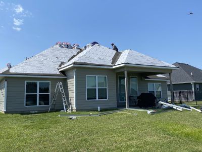 Damaged suburban house with torn roof and debris on the lawn under a clear blue sky