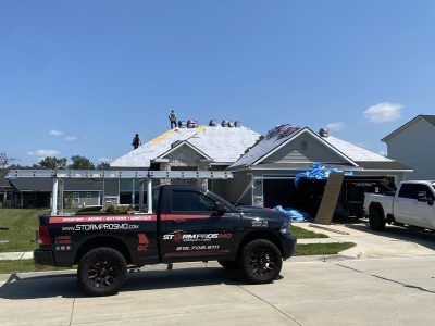 Workers on a roof with a black pickup truck in front of a suburban house under construction