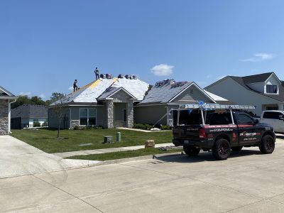 Suburban house with workers on the roof and a black SUV parked in the driveway
