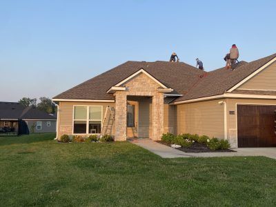 Suburban house exterior at sunset with a large green lawn and two workers on the roof