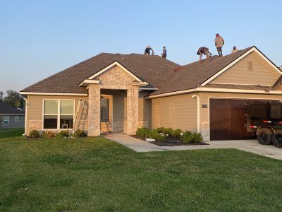 House with workers on the roof and garage, seen from the front lawn