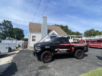 Black pickup truck parked in a gravel lot beside a white house under a blue sky