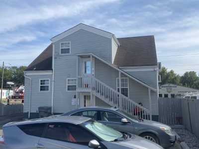 Gray house with exterior stairs and two parked cars in front under a clear sky