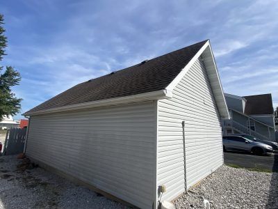 White garage with dark shingled roof beside gravel driveway under a blue sky