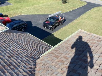 Driveway and lawn seen from a rooftop, with parked cars and a person’s shadow in the foreground