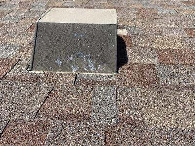 Rooftop vent with a concrete base on brown shingle roofing.