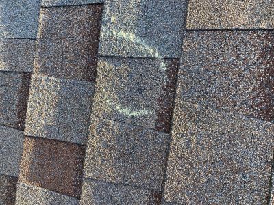 Close-up of weathered gray-brown roof shingles with patches of moss or discoloration