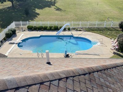 Backyard swimming pool with diving board, white fence, and grassy lawn behind it