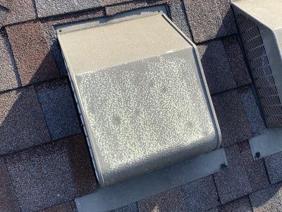Rooftop vent cap on gray asphalt shingles with a metal flashing base