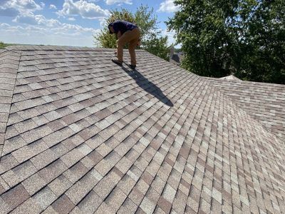 Person repairing shingles on a sloped roof under a bright sky