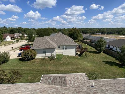 Suburban backyard view with a gray house, green lawn, and partly cloudy blue sky.