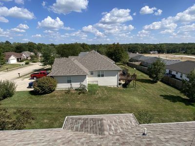 Suburban house with gray roof, green lawn, and a partly cloudy blue sky