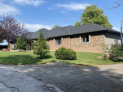 Single-story brick house with dark roof, driveway, lawn, and trees on a sunny day