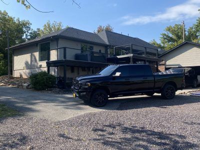 Black pickup truck parked in front of a two-story beige house on a gravel driveway.