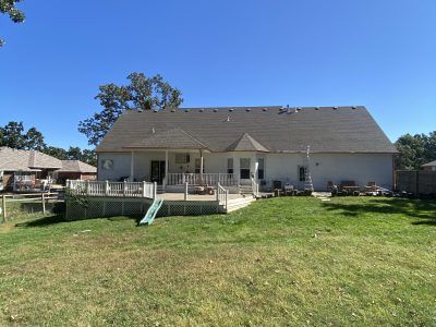 Backyard with a beige house, wooden deck, lawn, and a small play slide under a blue sky