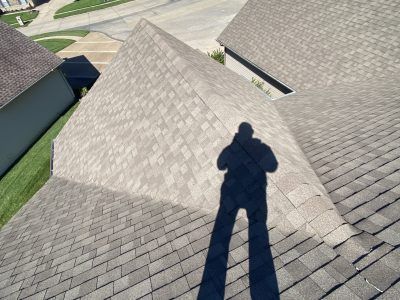 Shingled residential rooftops under bright sun, with a person’s shadow cast on the center roof.