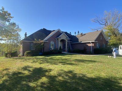 Brick suburban house with a front lawn, trees, and a clear blue sky