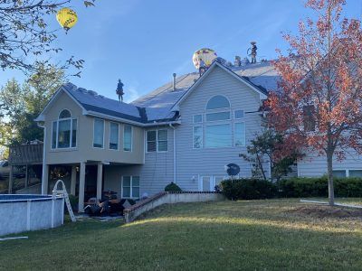 Suburban house with blue siding, white trim, and a covered patio beside a grassy yard and autumn tree.