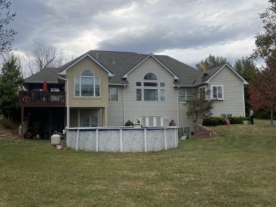 Large beige two-story house with deck and above-ground pool in a grassy backyard