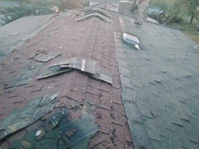 Rooftop with missing shingles and damaged red roof ridge under overcast light