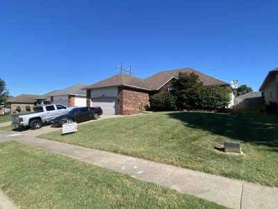 Suburban brick house with two parked vehicles and a sloped front lawn under a clear blue sky