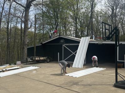 Workers installing metal siding on a black building in a wooded area