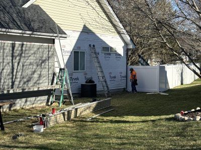 Workers painting the exterior of a white house, with ladders and supplies in the yard.