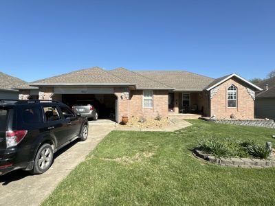 Suburban brick house with a black SUV in the driveway and a neatly trimmed front lawn