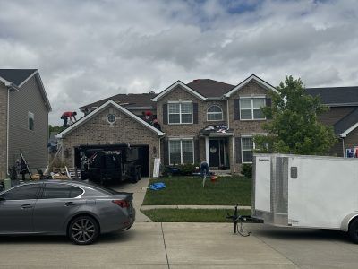 Suburban house with open garage, gray car parked in front, and white trailer on the street under cloudy skies