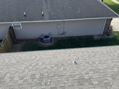 Rooftop view of a backyard with a house wall, air conditioner, fence, and small white object on the roof