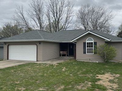 Single-story gray house with attached garage, front lawn, and bare trees under an overcast sky