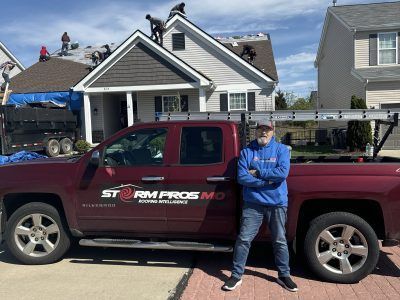 Man standing beside a maroon Storm Pros pickup truck in a residential driveway