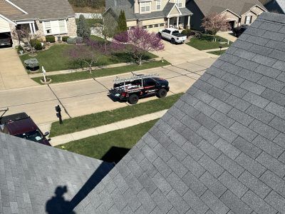 Suburban street view from a rooftop, with parked vehicles, sidewalks, lawns, and houses.
