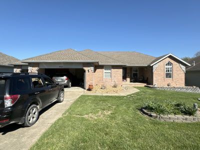 Suburban brick house with a black SUV in the driveway and a green lawn under a clear blue sky