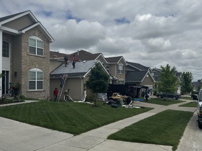 Suburban neighborhood with people working on a house roof and driveway under a cloudy sky