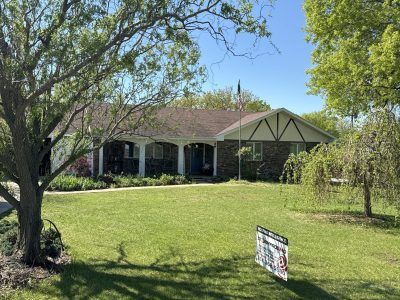 Single-story house with a front porch, large lawn, and a real estate sign in the yard