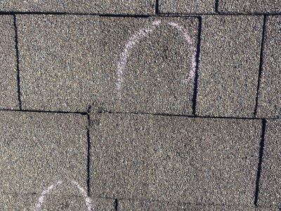 Close-up of dark gray roof shingles with two faint white chalk marks