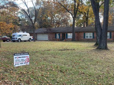 Suburban brick house with white pickup, autumn trees, and a yard sign in the front lawn